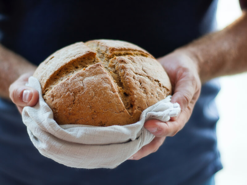 Two hands holding a round loaf of sourdough bread.