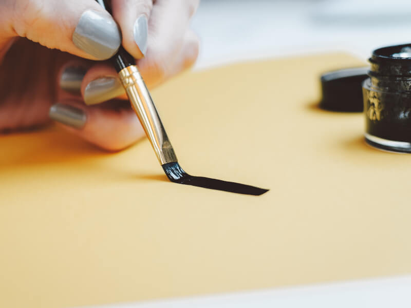 Someone using a calligraphy brush to write black ink on yellow paper.