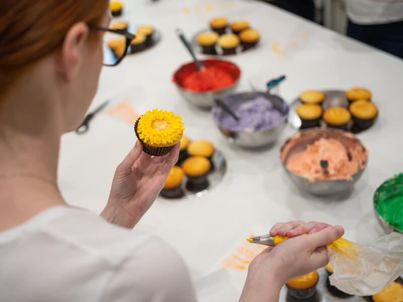 A person is standing at a table decorating cupcakes with different coloured icing