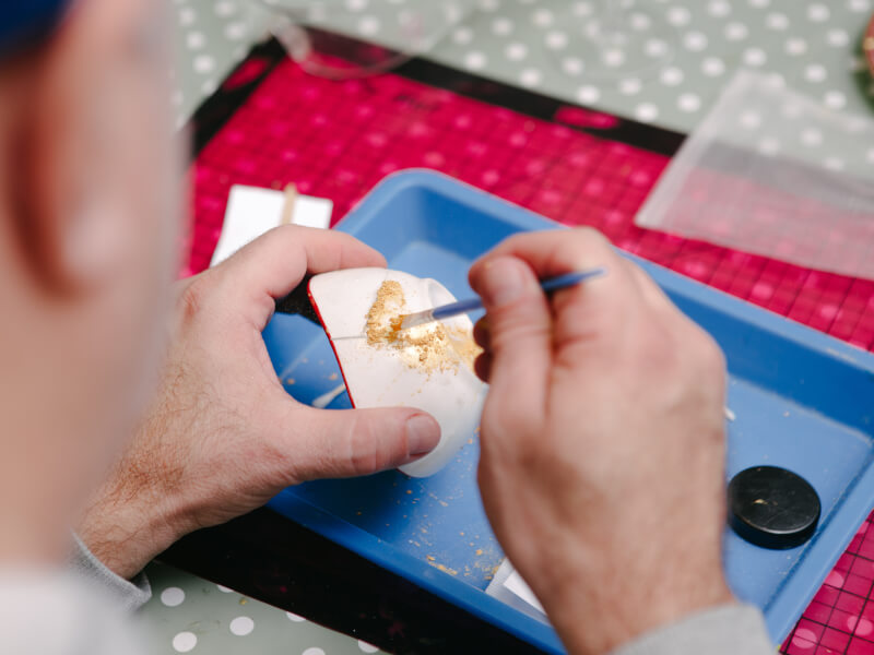 A close up of a person brushing gold powder onto a repaired piece of pottery