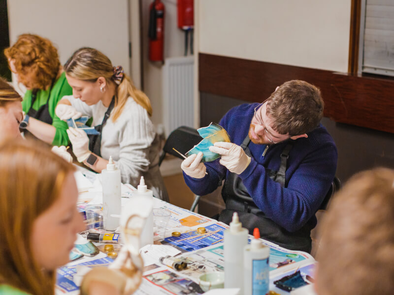 A group of people are sitting around a table, learning how to repair pottery using kintsugi technqiues