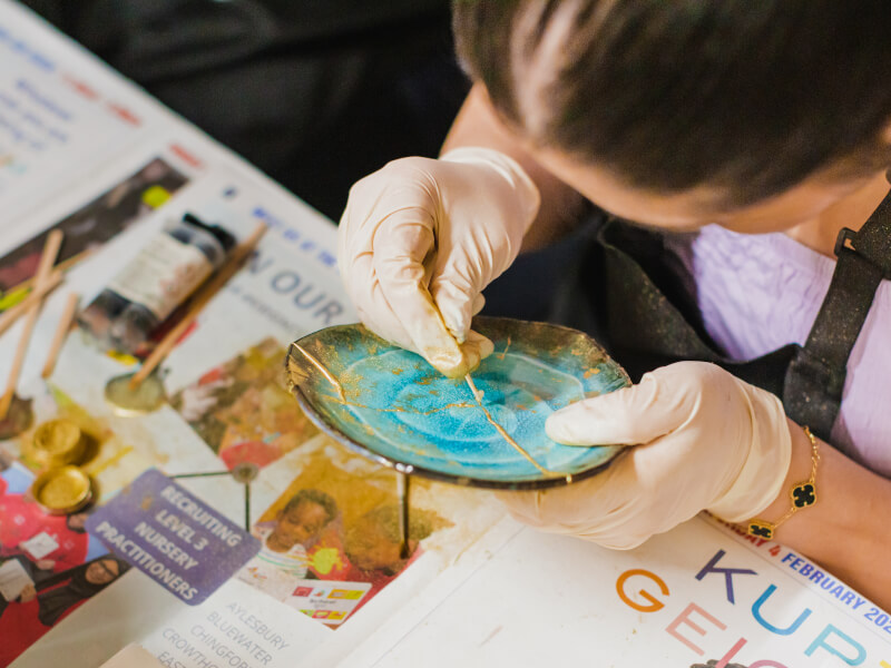 A close up of a person repairing a turquoise plate with gold lacquer and powder