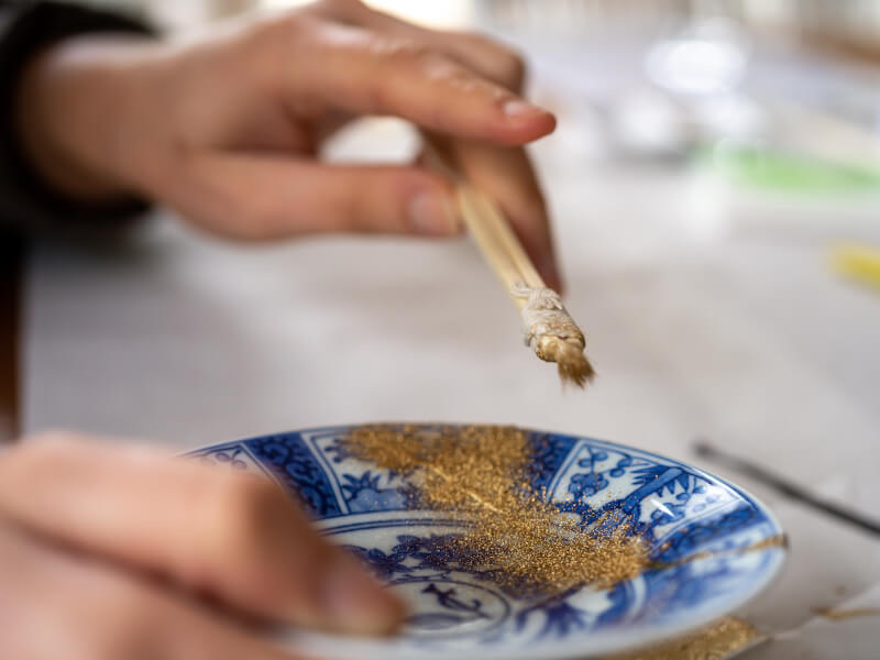 A close up of a person applying gold powder to a kintsugi project with a paintbrush