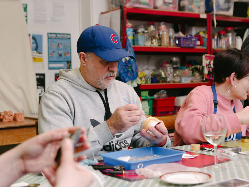 A man sits at a table, repairing pottery with gold adhesive at a kintsugi class