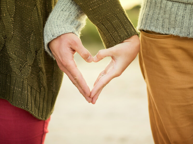 A couple form a heart shape with their hands.