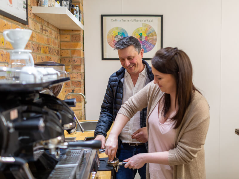 A man smiles while learning from his teacher at a latte art class