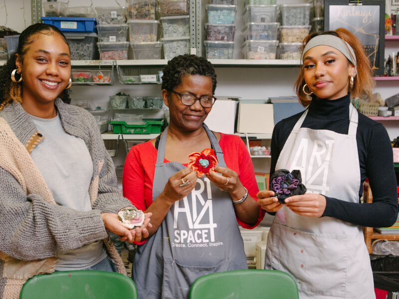 Three women are smiling and holding hand sewn fabric corsages they've made