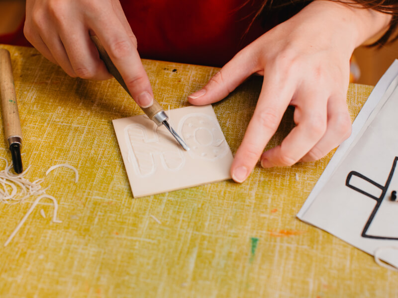A close up of a person carving a lino block with a lino carving tool