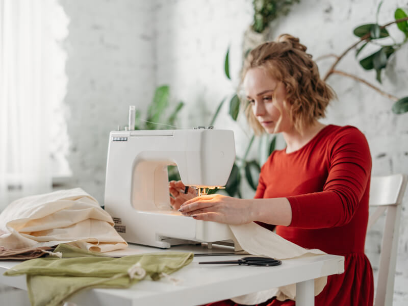 A woman in a red dress is sewing beige fabric using a sewing machine