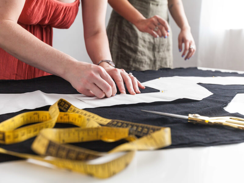 A woman is leaning over a table, tracing a sewing pattern onto black fabric 