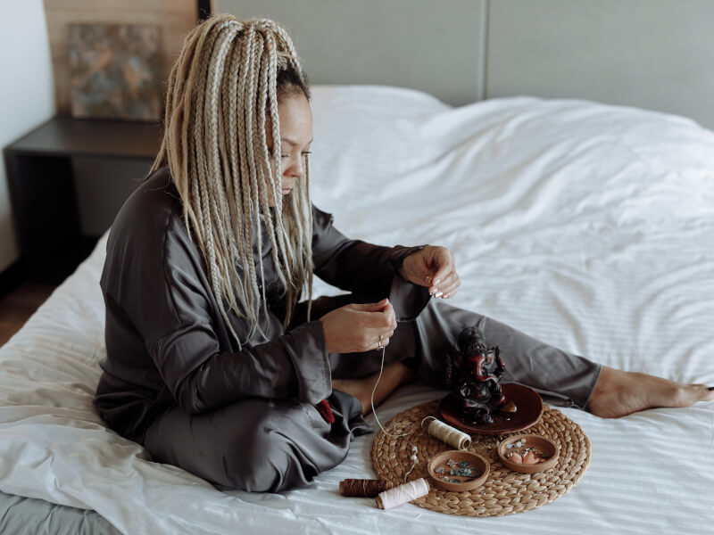 A woman is sitting on a bed, hand sewing a project
