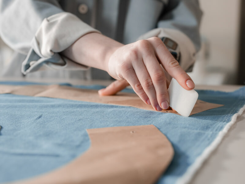 A person is tracing a sewing pattern onto blue fabric