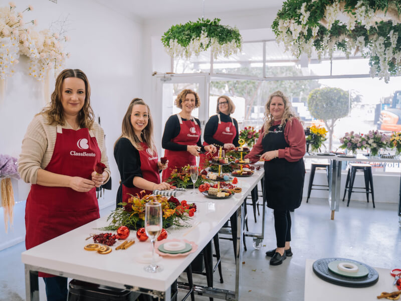 A group of people stand at a table at a flower wreath class in London as they learn to make wreaths