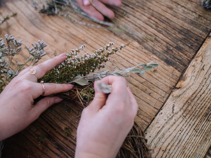 A close up of a person adding dried flowers to a wreath base