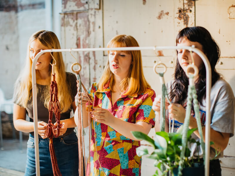 A teacher is showing two girls how to make DIY macrame planter in coloured cord