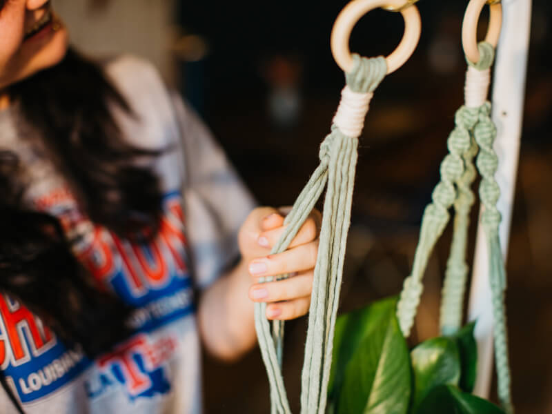 A close up of a woman tying macrame knots in green cord to make a DIY planter