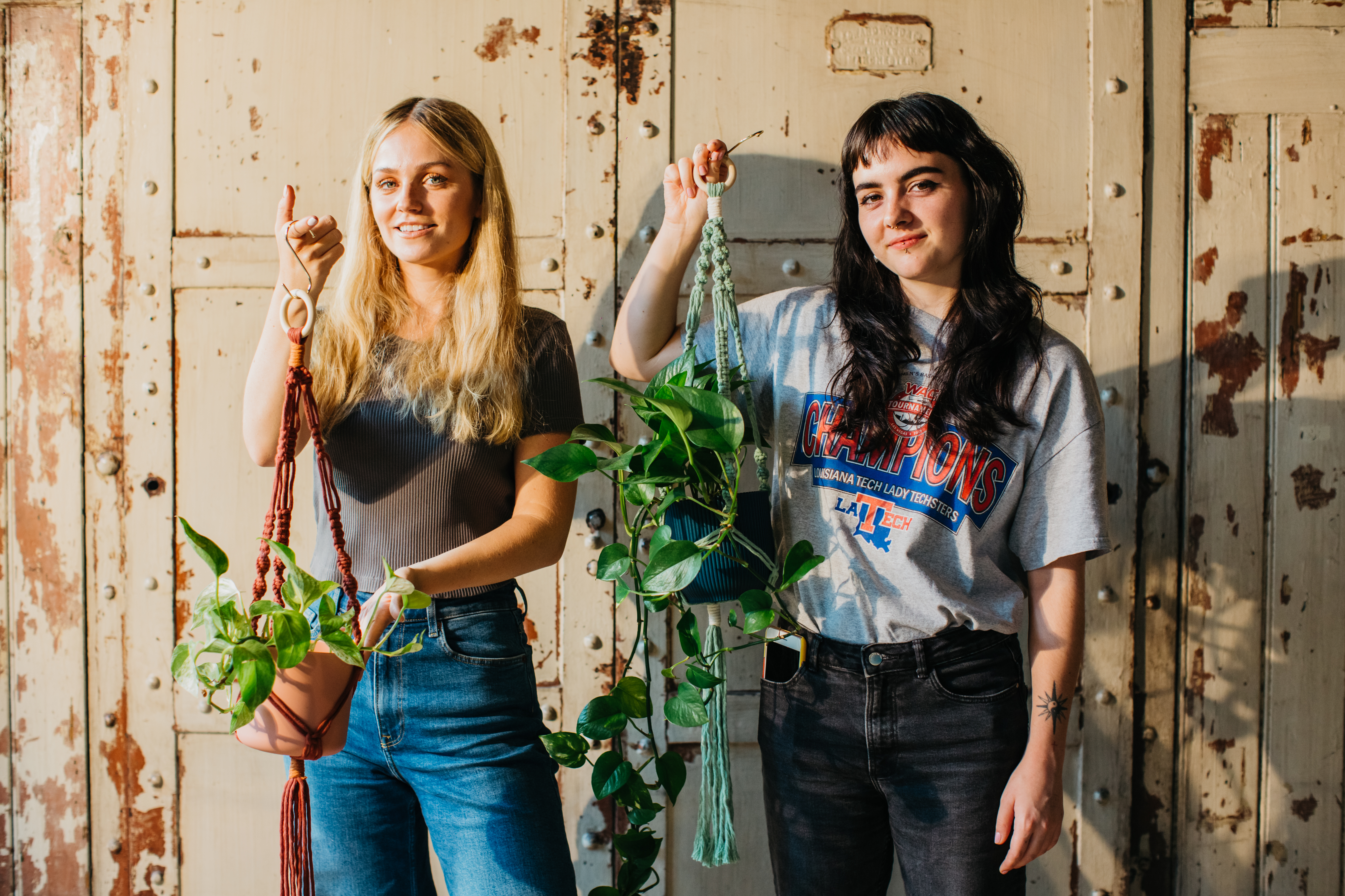 Two women are holding handmade macrame hanging planters and smiling