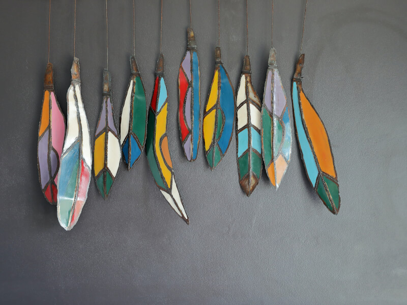 A row of painted metal feather decorations hang on a dark grey wall