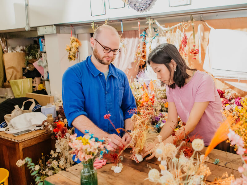 A man and woman are making ikebana arrangements in a room full of flowers
