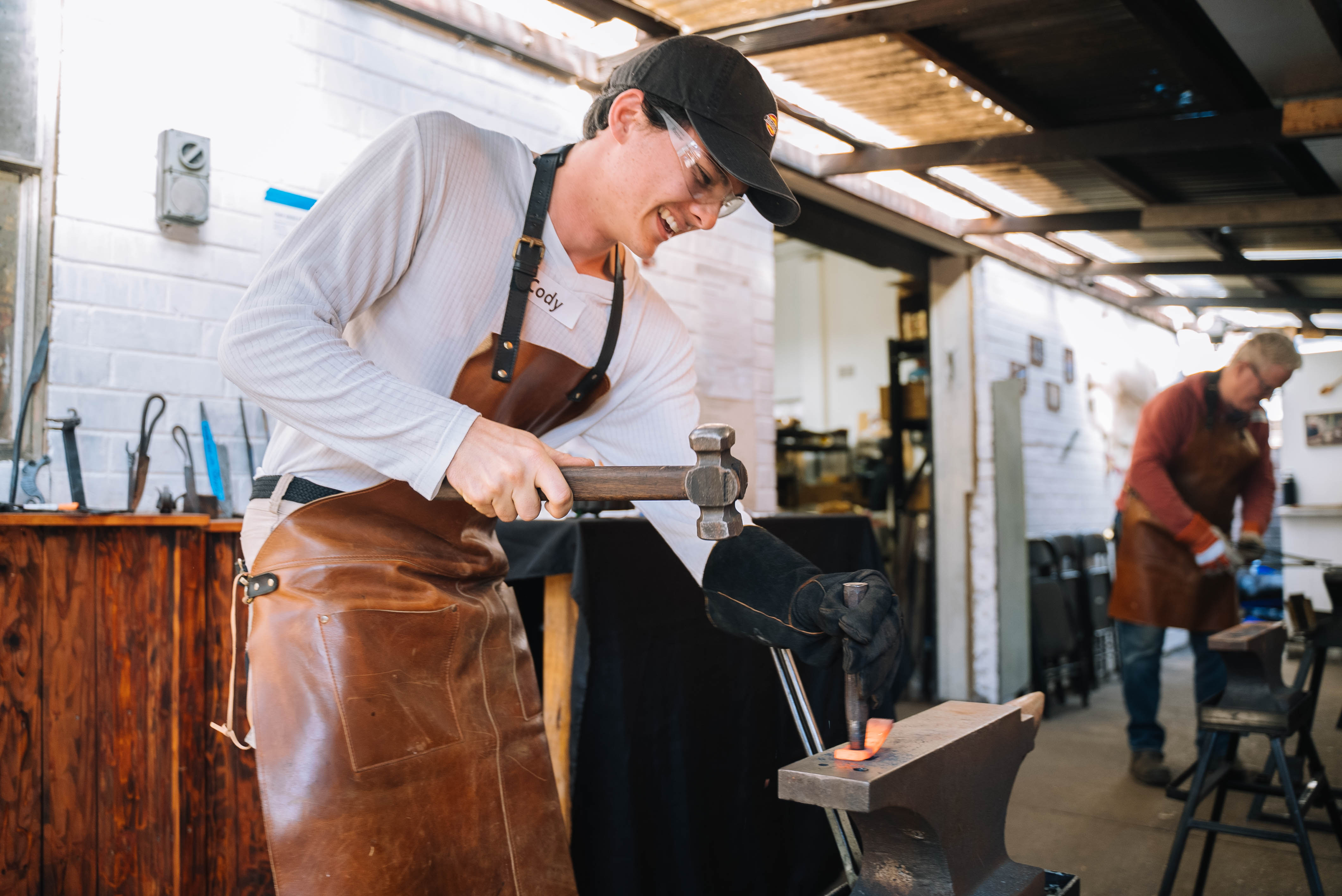 A man is trying blacksmithing, hammering molten metal