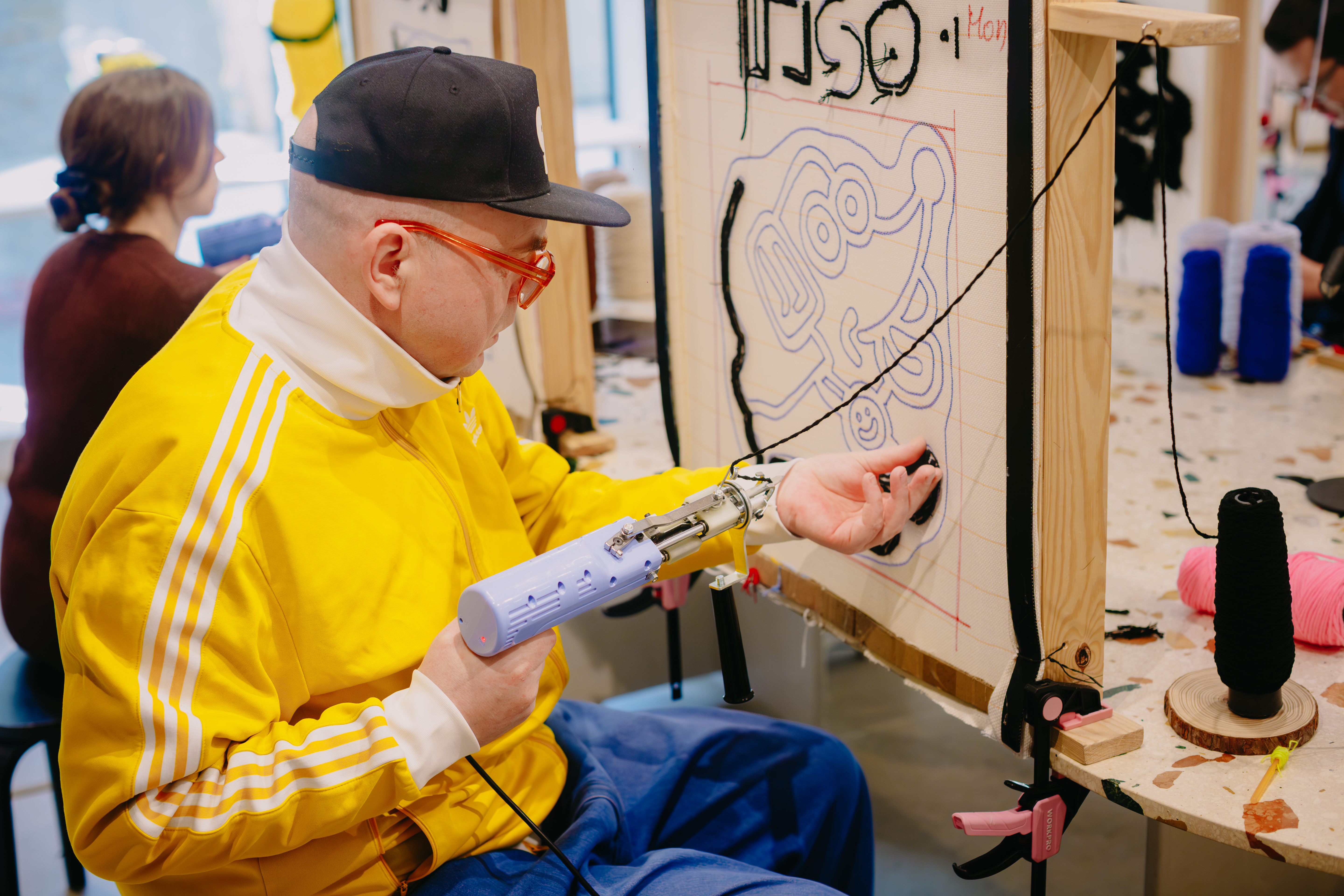 A man is sitting at a canvas, creating a hand tufted rug using a tufting gun