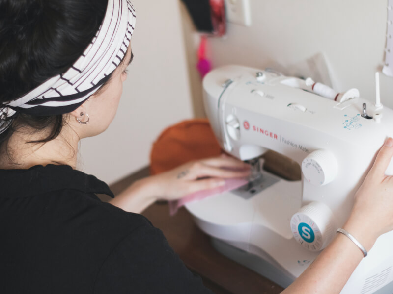 A woman sits at a sewing machine, stitching pink fabric