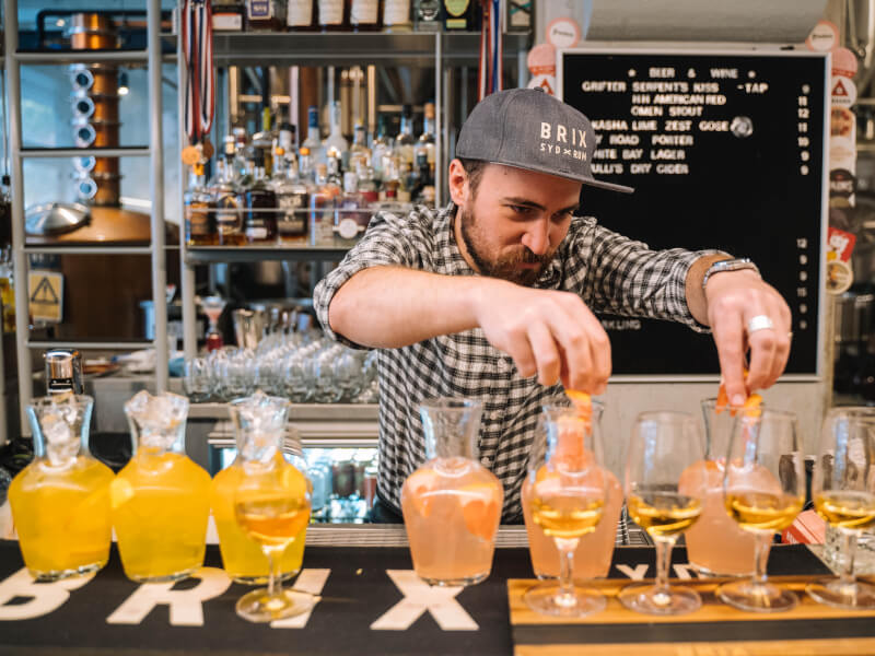 A man behind a bar is adding garnishes to glasses with spirits in them