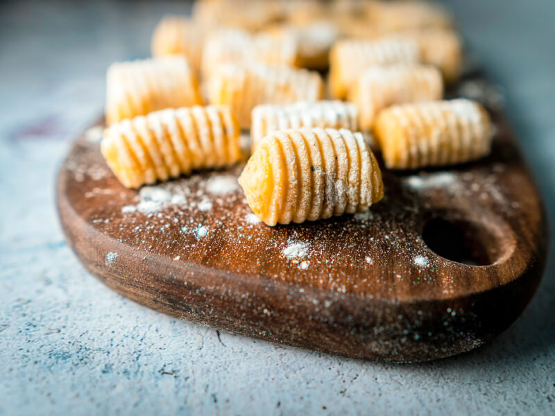 A wooden chopping board on a blue table, with homemade gnocchi sitting on top in two rows