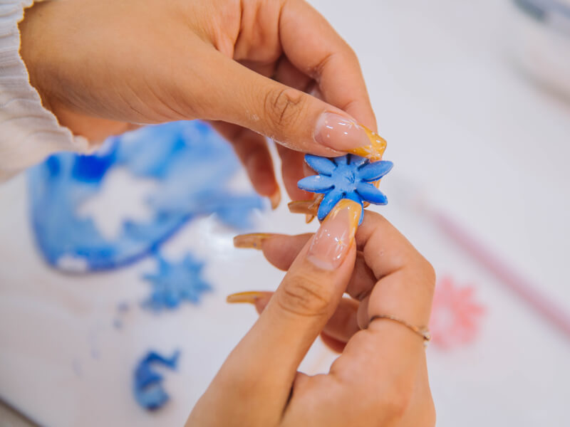 A close up of a person holding handmade blue clay flower