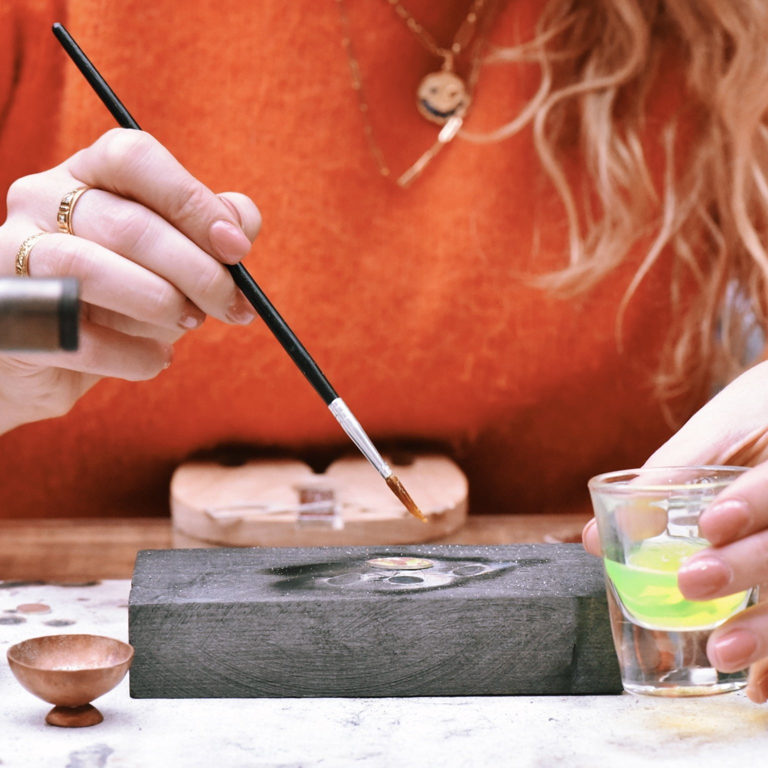 Close up of a person at a jewellery class using a paintbrush to add chemicals to a silver pendant