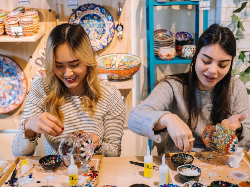 Two women smile as they make mosaic lamps