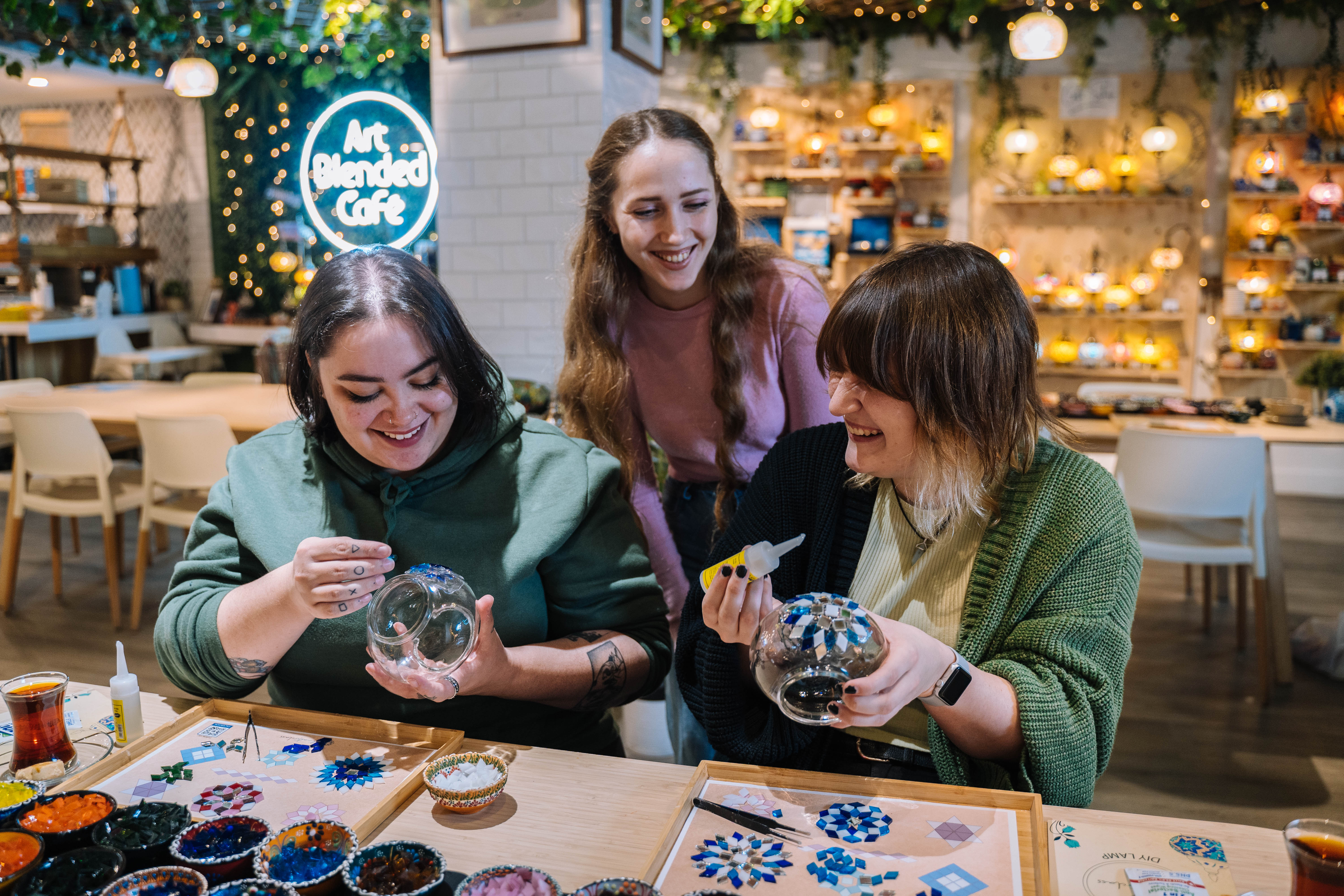 A woman is teaching two other women to make mosaic glass lamps