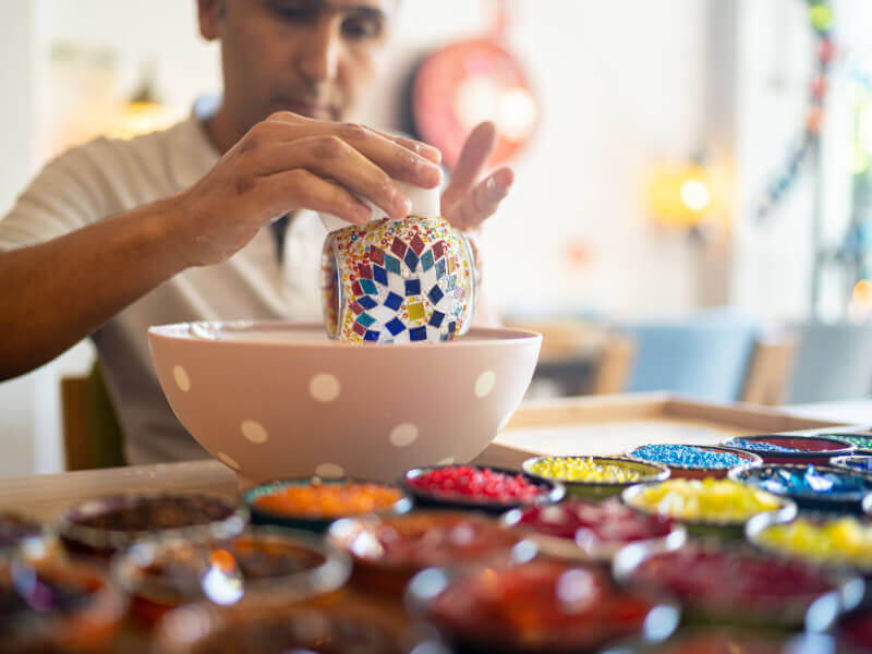 A man is making a mosaic design on a pot at a craft class