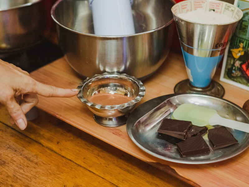 A person is pointing to ingredients on a table for making handmade chocolate