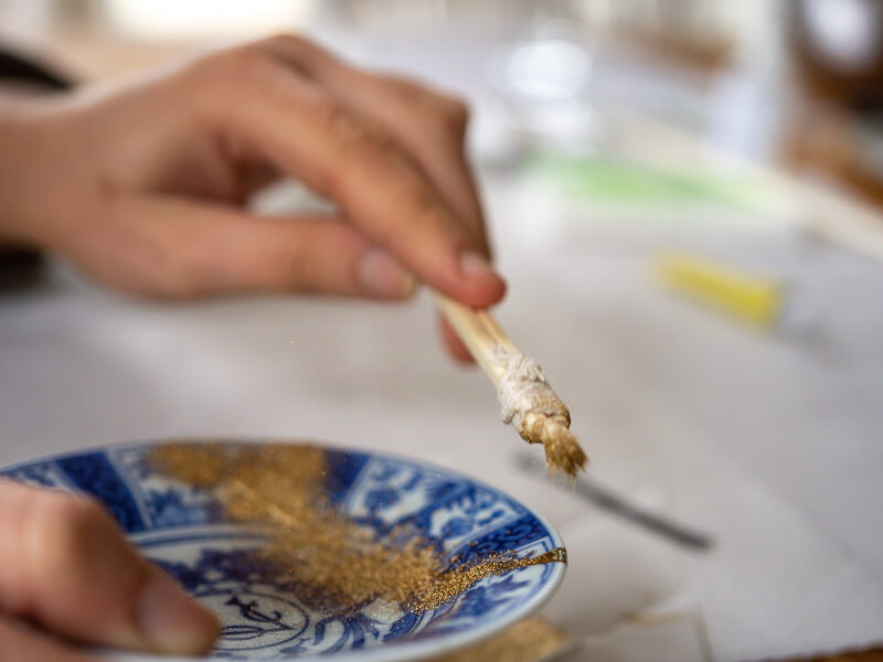 A person is using gold powder on a blue plate in a kintsugi project