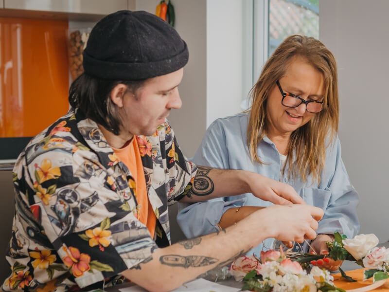 A woman and young man are making a floral wreath decoration