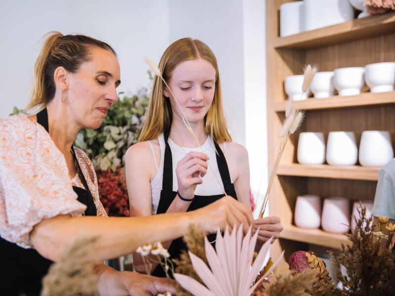 A woman and young girl are creating a dried floral arrangement 