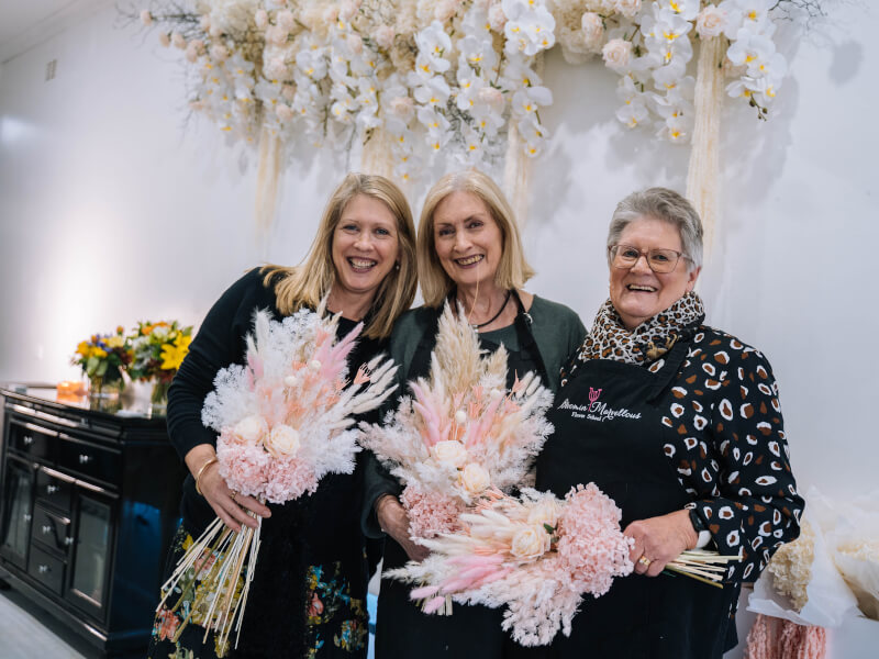 Three women are laughing and holding hand tied pink bouquets