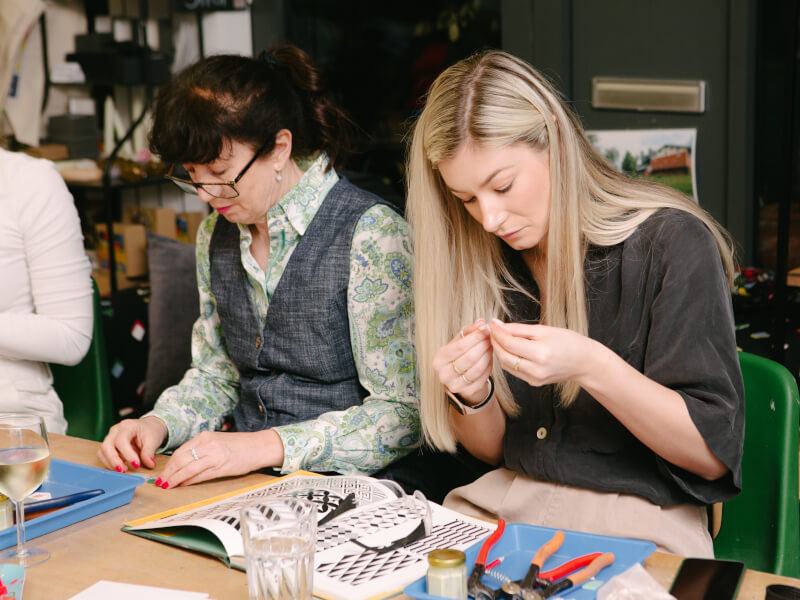 Two women are sitting at a table, making mosaic designs from coloured tiles