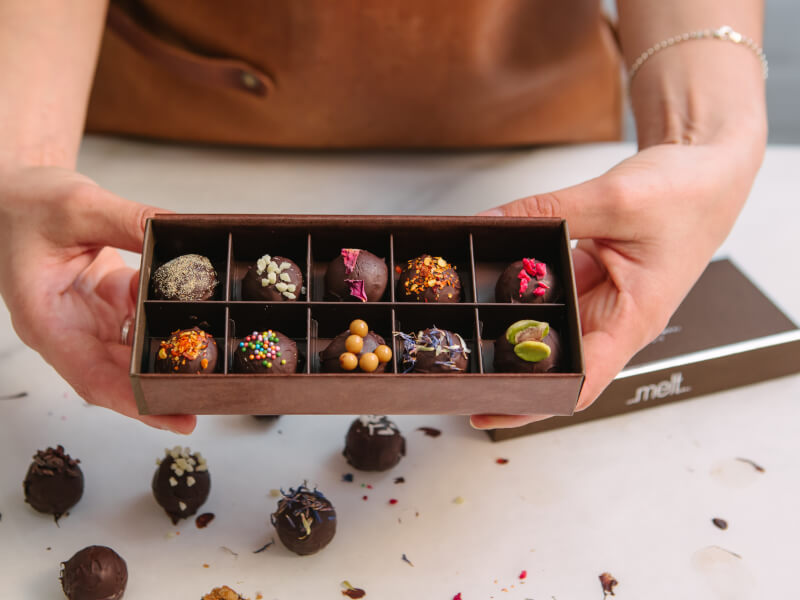 A close up of a handmade box of chocolate truffles, finished with nuts and sprinkles
