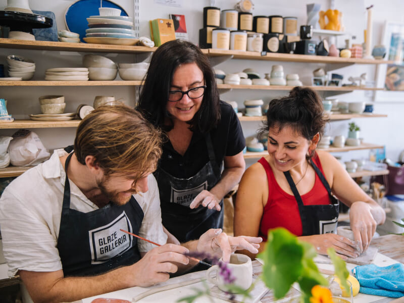 A young man and woman are being taught pottery making by an artist