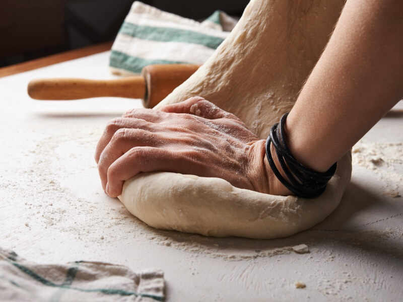 A person kneads dough on a floured worktop.