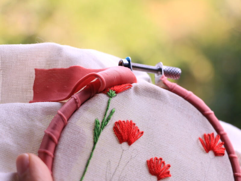 A person using embroidery to decorate pink fabric with flowers made from red and green thread