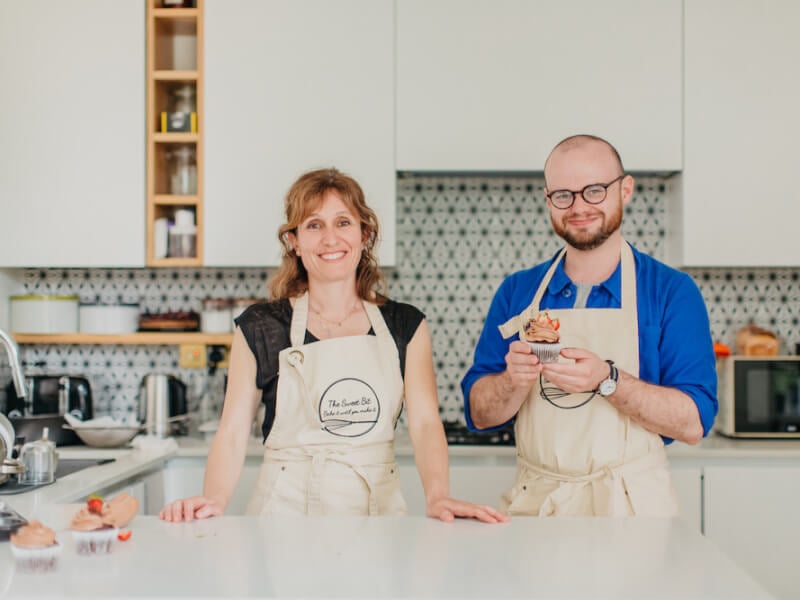 A man and women smile in a kitchen with homemade chocolate cupcakes topped with strawberries