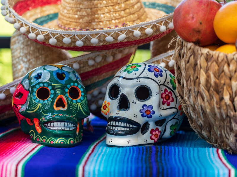 Two day of the dead style painted skulls on a bright table cloth.