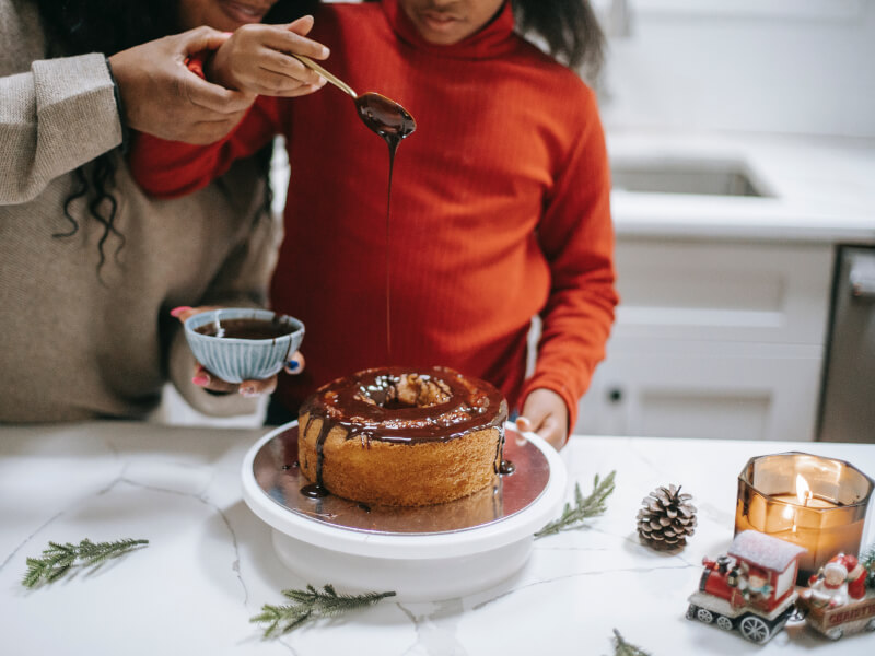 Child spooning homemade chocolate onto a cake. 