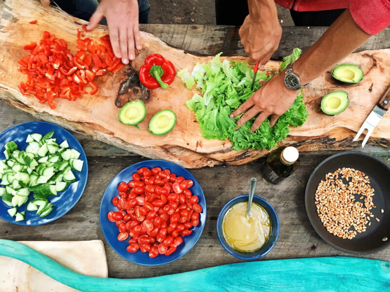 Two people preparing and chopping vegetables on a wooden chopping board