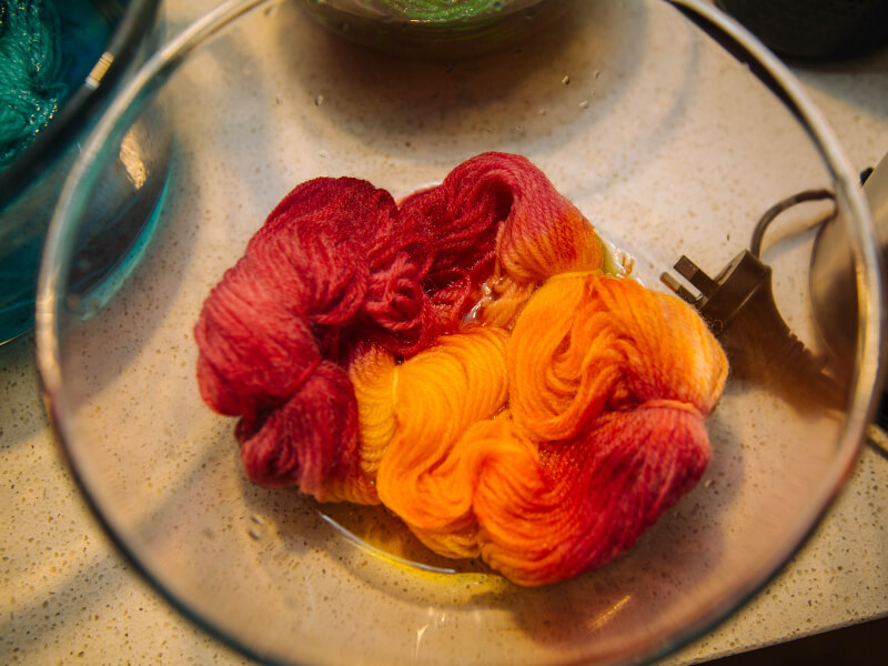 Orange hand-dyed yarn sits in a glass bowl