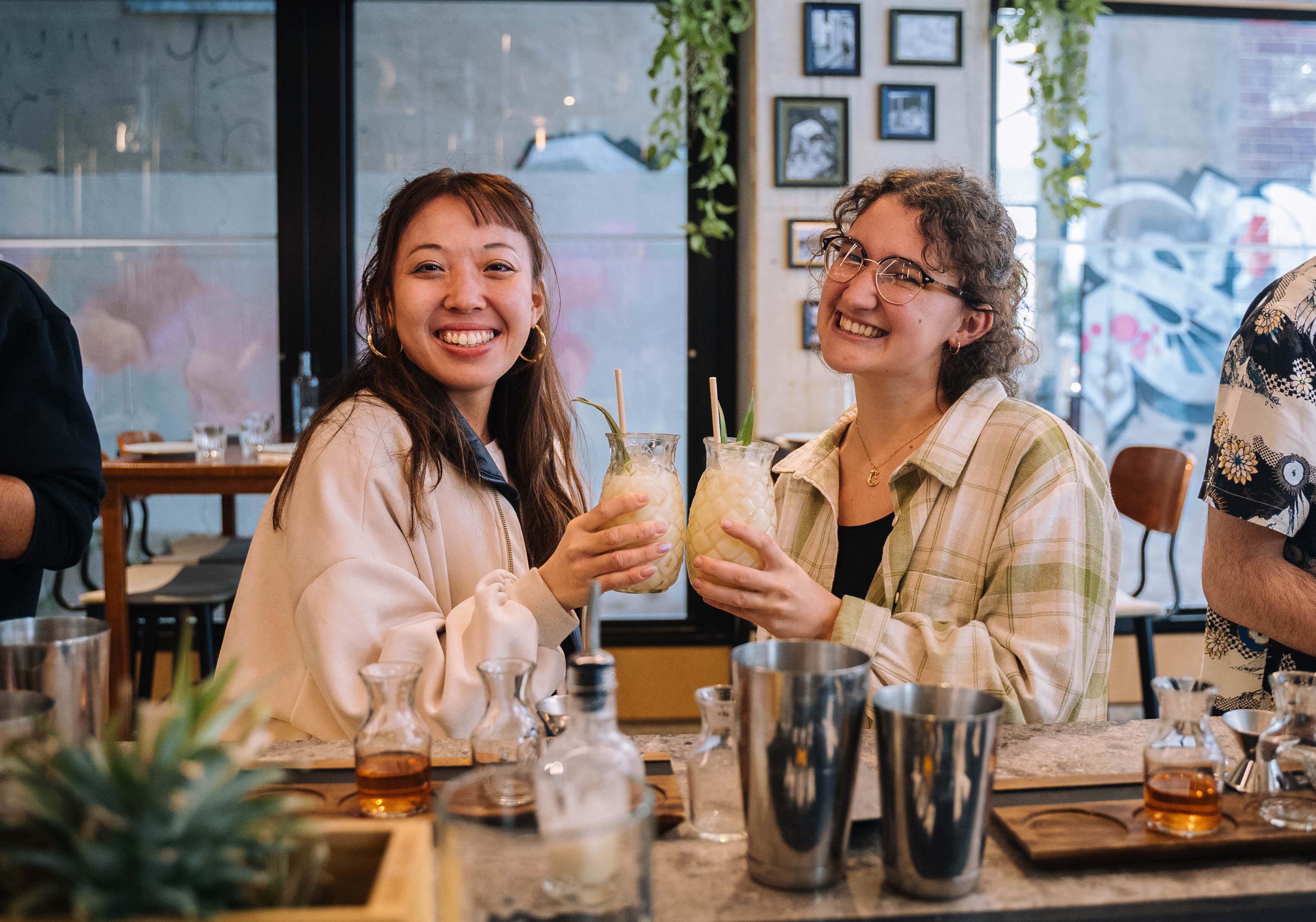 Two women are smiling and clinking glasses at a paint and sip evening