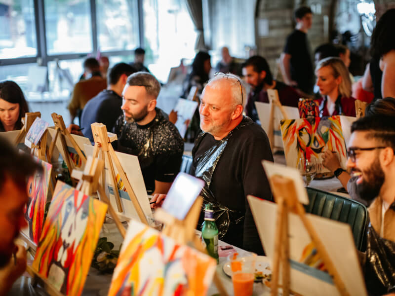 A room filled with people sitting at easels, painting brightly coloured pictures of a lion